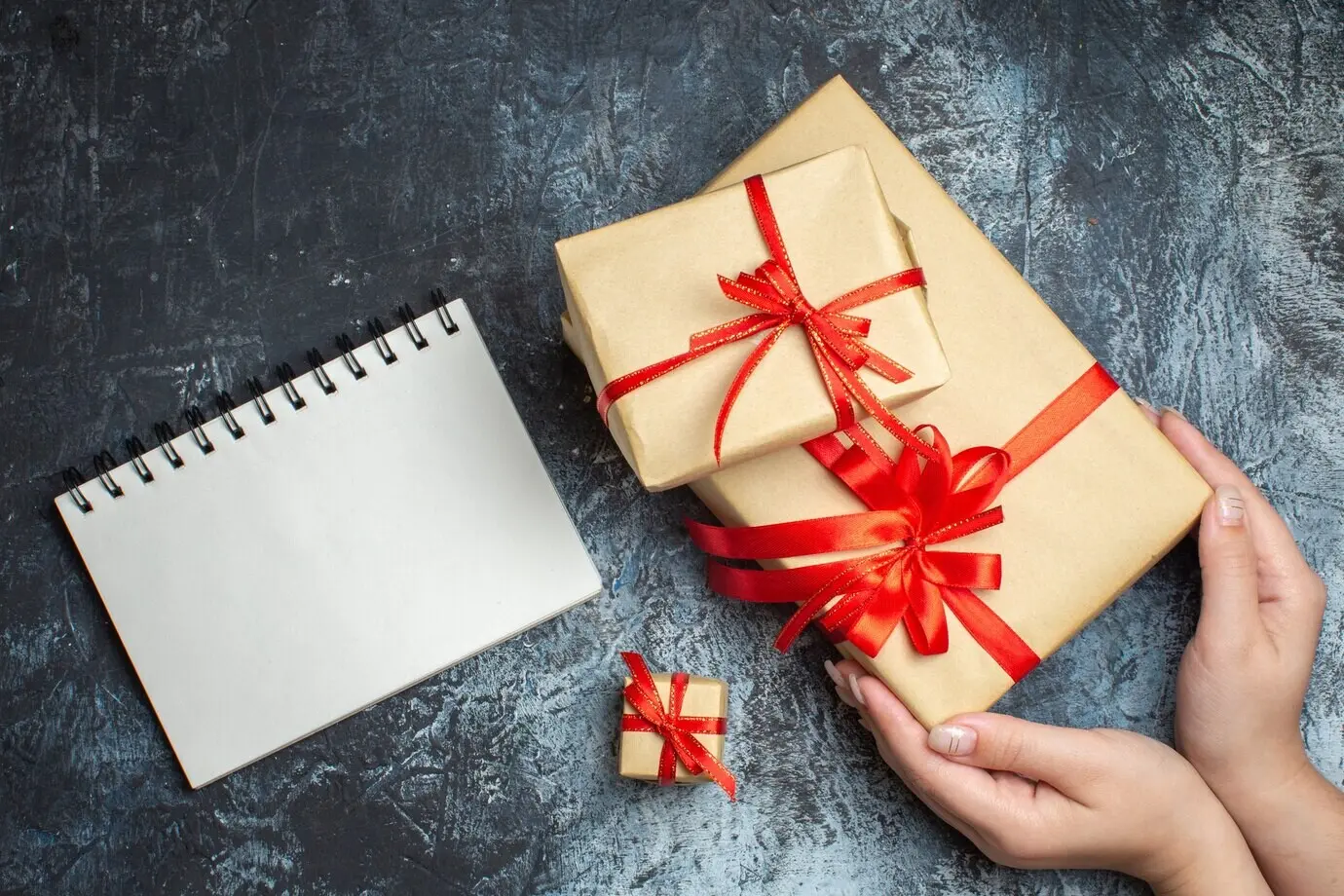 Overhead view of Christmas presents tied with red bows on a light-and-dark background.
